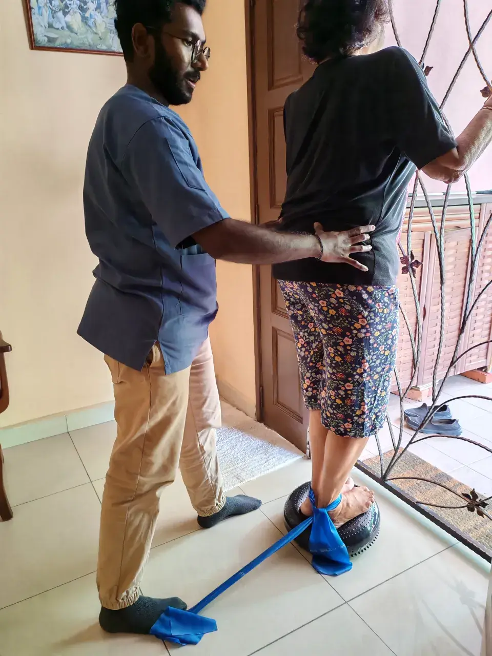 Physiotherapist supporting a patient with standing balance rehabilitation at home